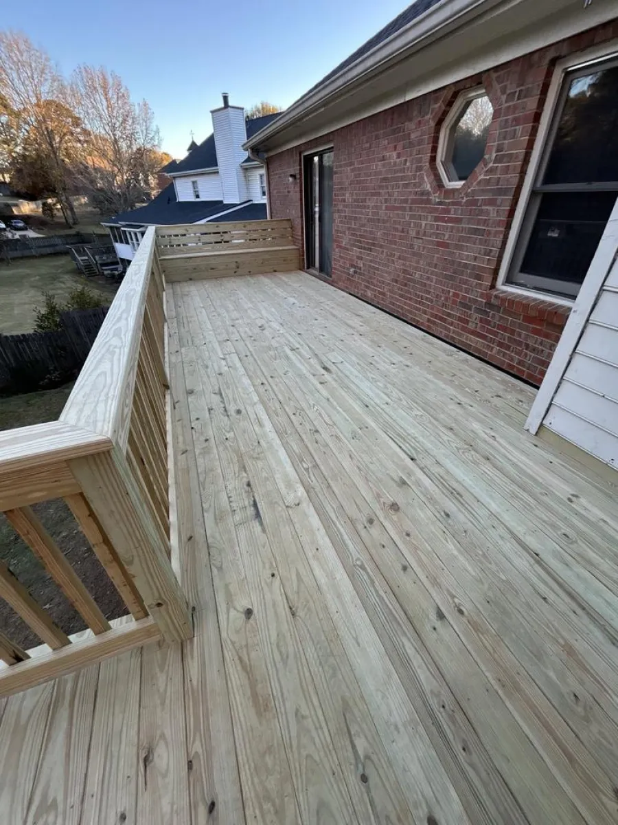 Newly built wooden deck attached to a brick house with railing and bench seating on the side.