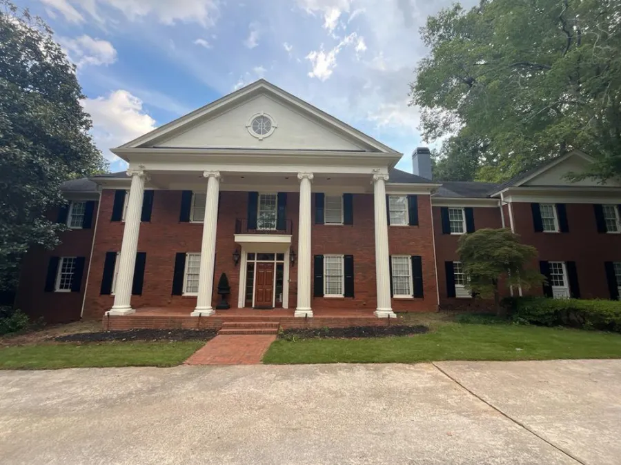 Front view of a large red brick colonial house with white columns and black shutters under a blue sky.