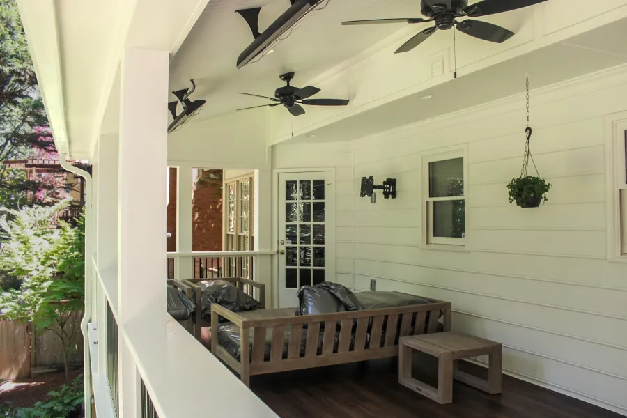 Cozy covered porch with wooden furniture, ceiling fans, hanging plant, and white siding under natural light.