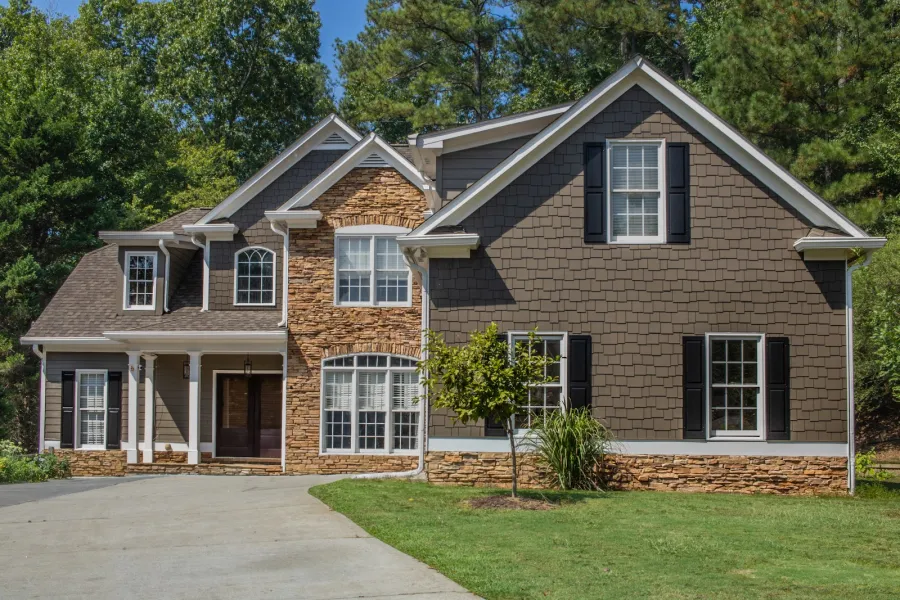 Close-up of a beige house exterior with dormer windows and gray shingles on a sunny day.