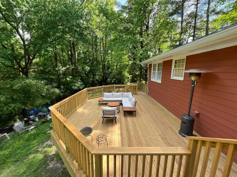 Newly built wooden deck attached to a house with brown siding and surrounding trees in the background