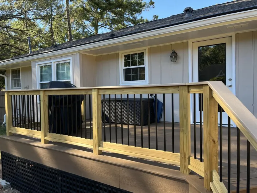 Green house exterior with white garage door, black window shutters, surrounded by trees and blue sky.