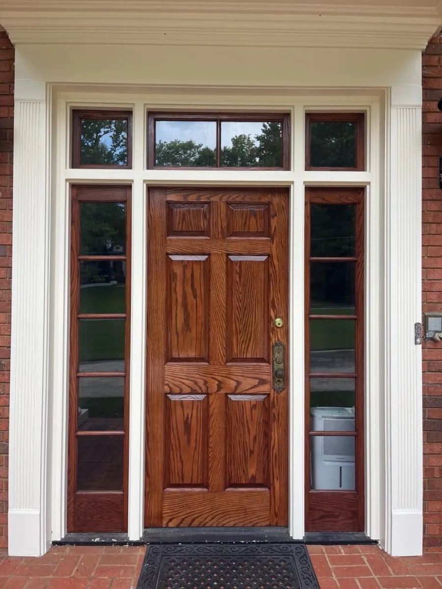 Classic wooden front door with decorative glass sidelights and transom framed by white molding on brick exterior.