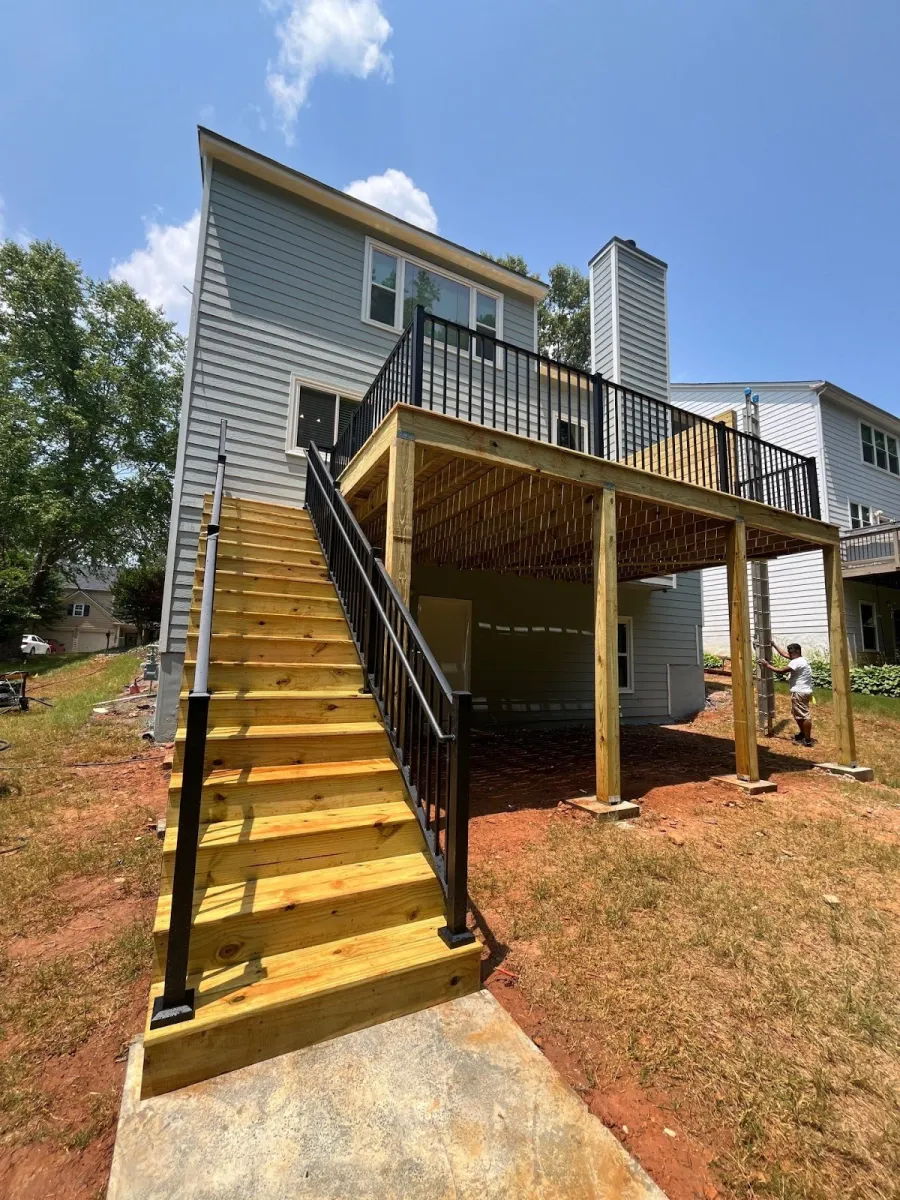 New wooden outdoor staircase and raised deck with black metal railing attached to gray house on sunny day.