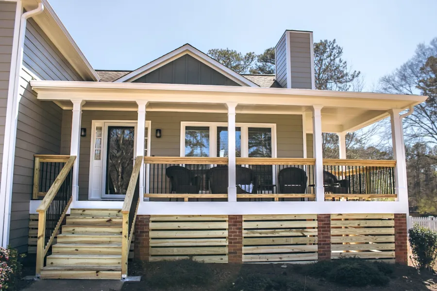 Modern front porch with wooden stairs, white columns, black chairs, and gray siding under clear sky