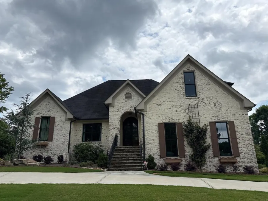 Large white brick house with dark roof, arched front door, steps, and manicured lawn under cloudy sky.