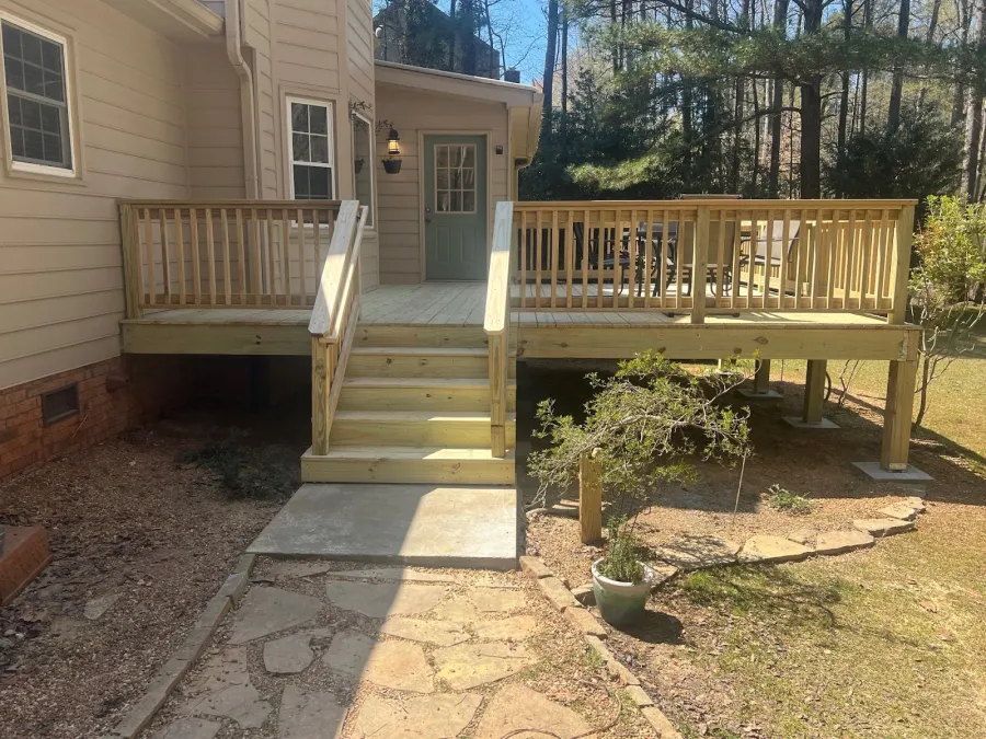 Newly built wooden deck with stairs and railing attached to beige house under bright sunlight.
