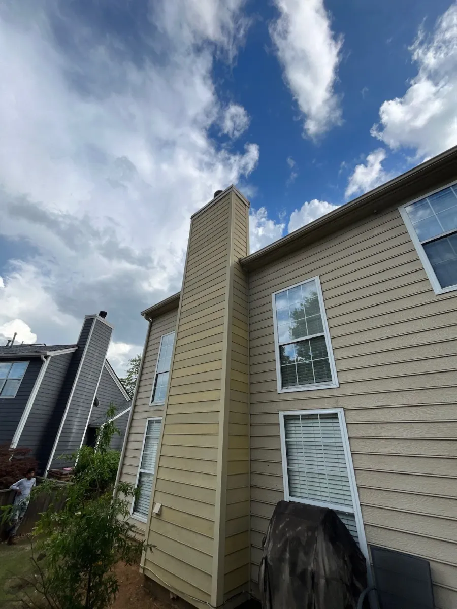 Close-up of a beige house exterior with dormer windows and gray shingles on a sunny day.