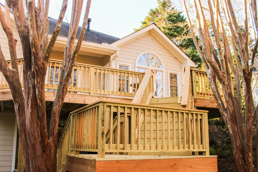 Green house exterior with white garage door, black window shutters, surrounded by trees and blue sky.