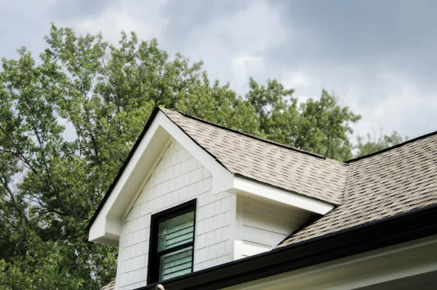 Two-story white house with green roof, front porch, stairs, surrounded by bushes and a clear blue sky.