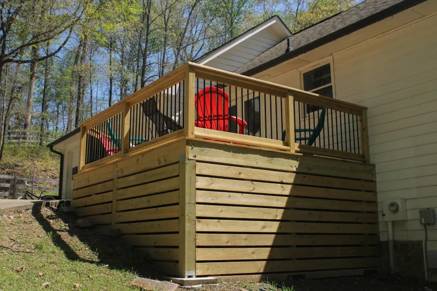 Outdoor wooden deck with stairs and black metal railings in natural backyard setting during daytime