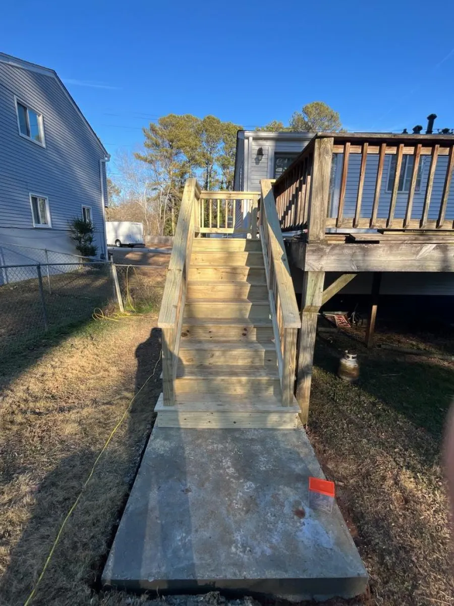 New wooden stairs with railings leading up to a raised deck attached to a house, under clear blue sky.