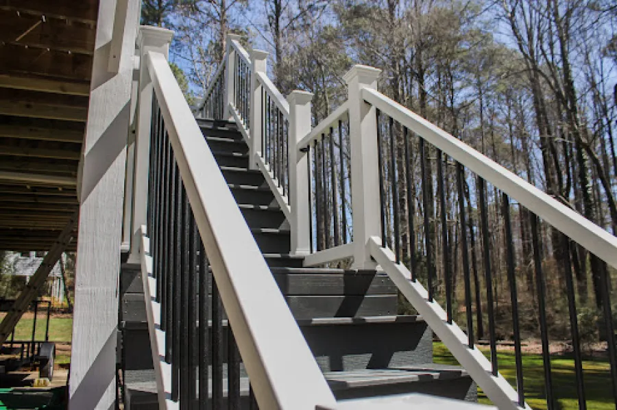 Outdoor staircase with white railings and black balusters leading up to a wooden deck on a sunny day.