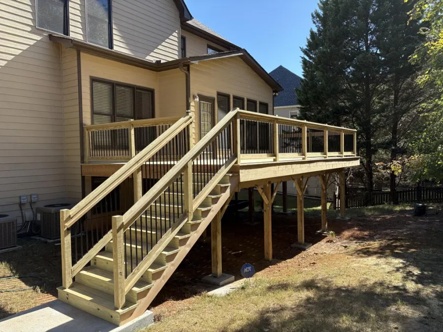 Green house exterior with white garage door, black window shutters, surrounded by trees and blue sky.