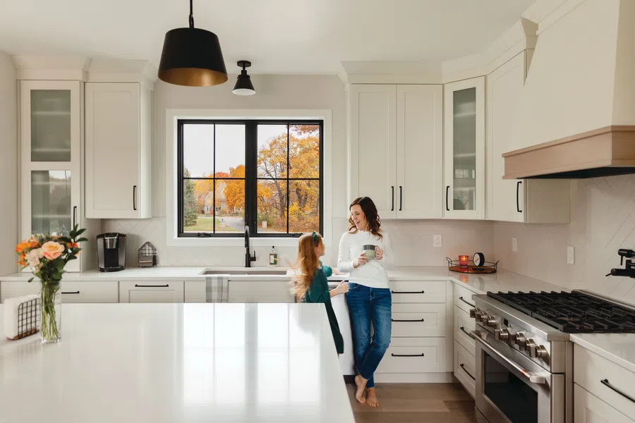 Mother and daughter chatting in a modern white kitchen with large island and autumn trees outside window