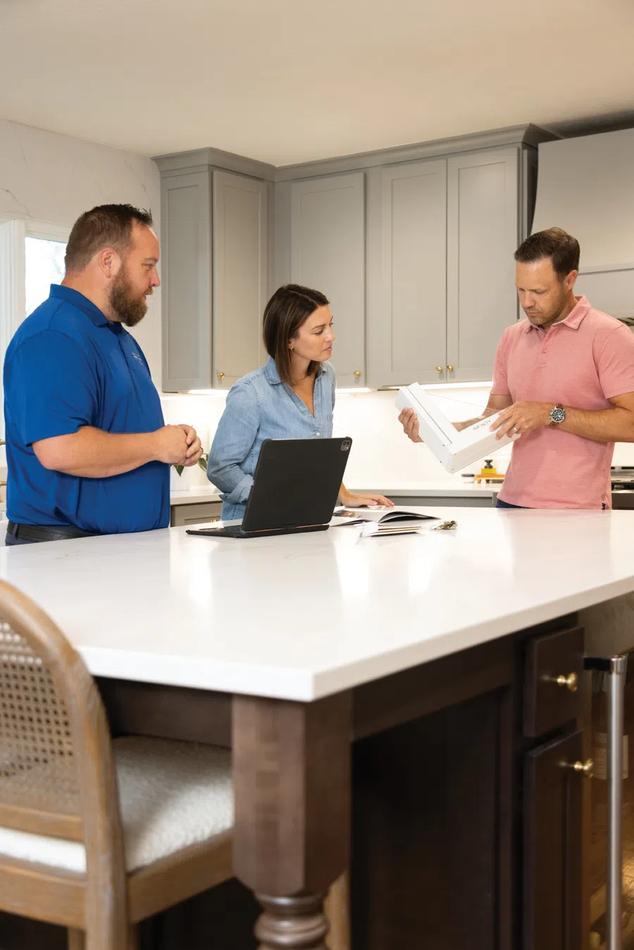 Three people discussing a product in a modern kitchen with gray cabinets and white countertop.
