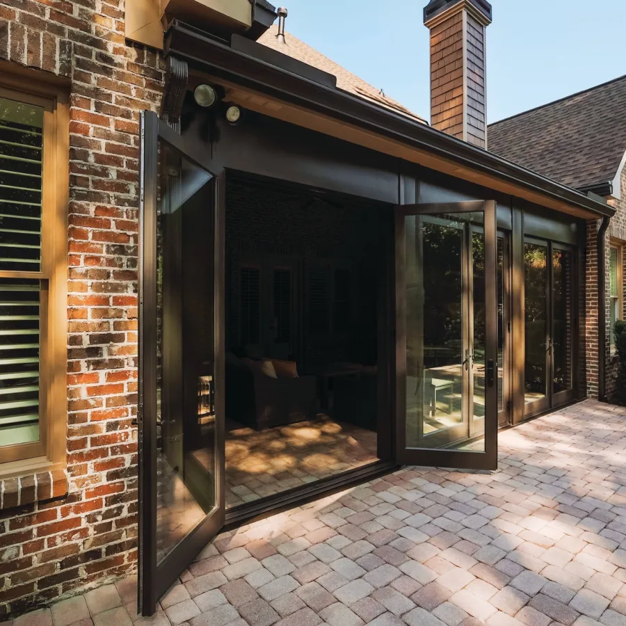 Spacious brick patio with large glass doors opening to a cozy living room in a suburban home.