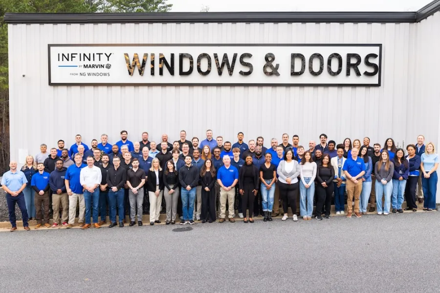 Large diverse group of employees posing outside building with Infinity Windows & Doors sign