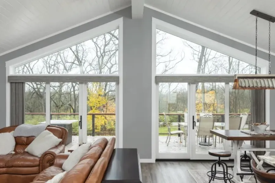 Modern living room and dining area with large glass doors opening to a patio overlooking autumn trees.