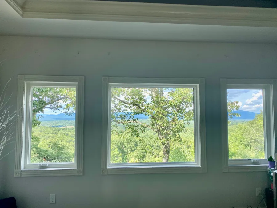 Three large windows offering a scenic view of lush green trees and distant mountains on a clear day.
