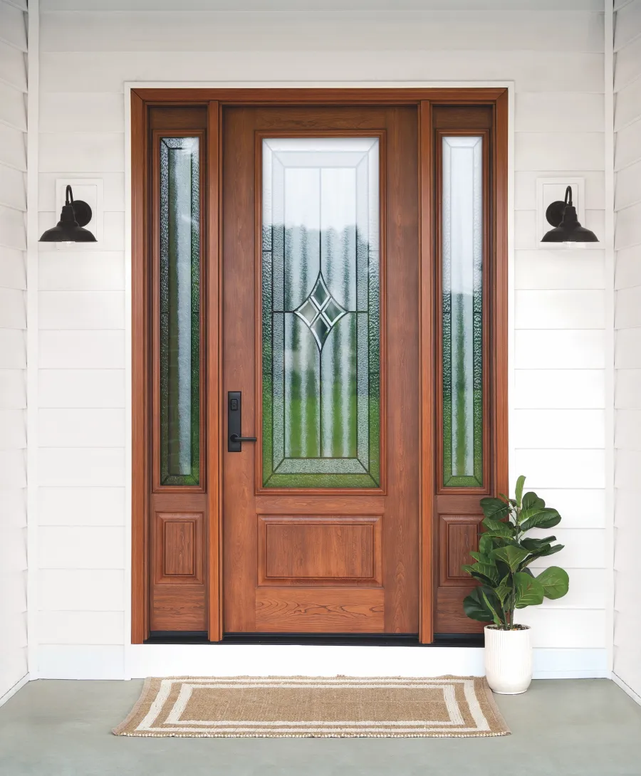 Wooden front door with decorative glass panels, black handles, flanked by two black wall lamps and a potted plant.