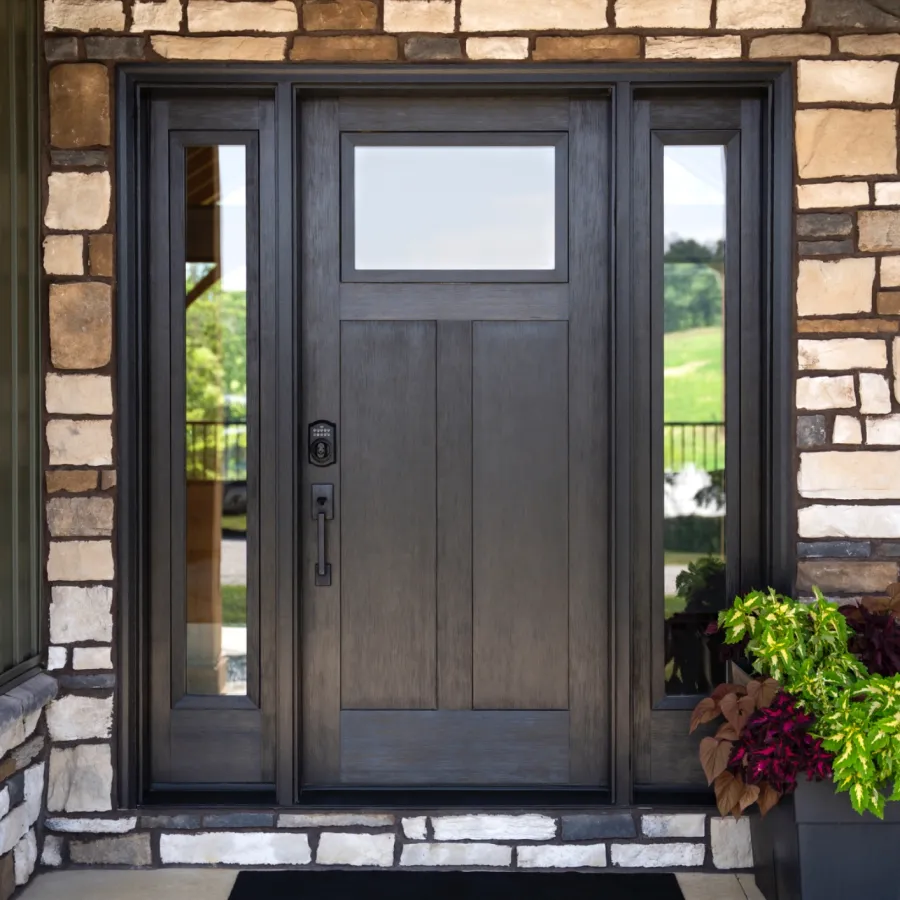 Modern dark wooden front door with side glass panels set in stone wall with potted plants.