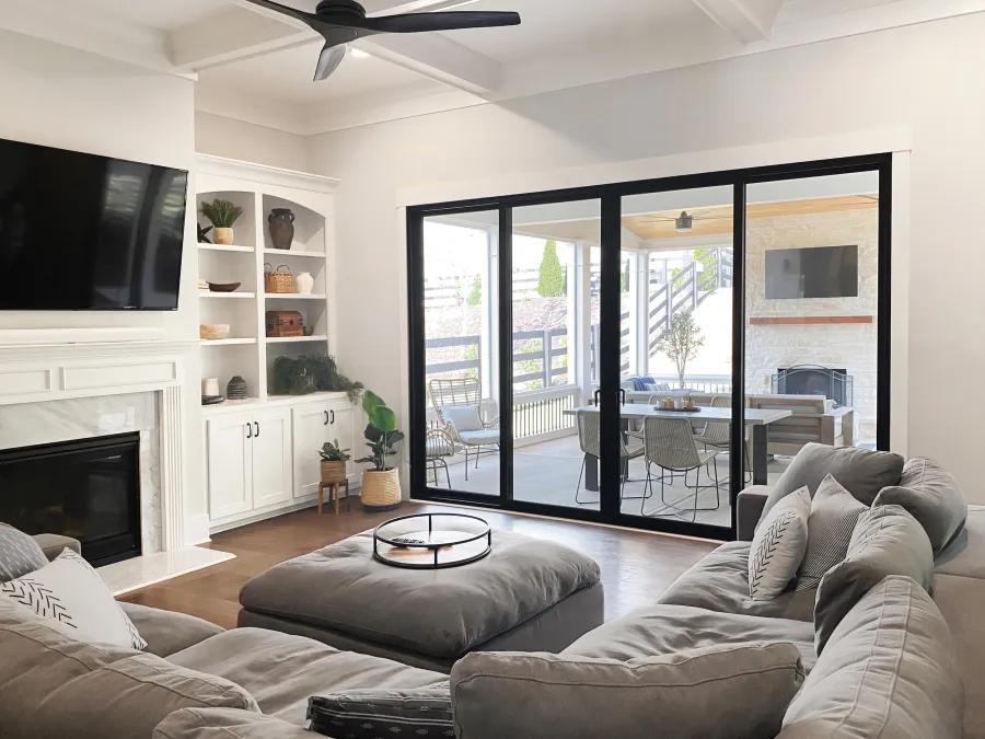 Bright modern living room with gray sectional sofa, fireplace, built-in shelves, and glass sliding doors to outdoor patio.