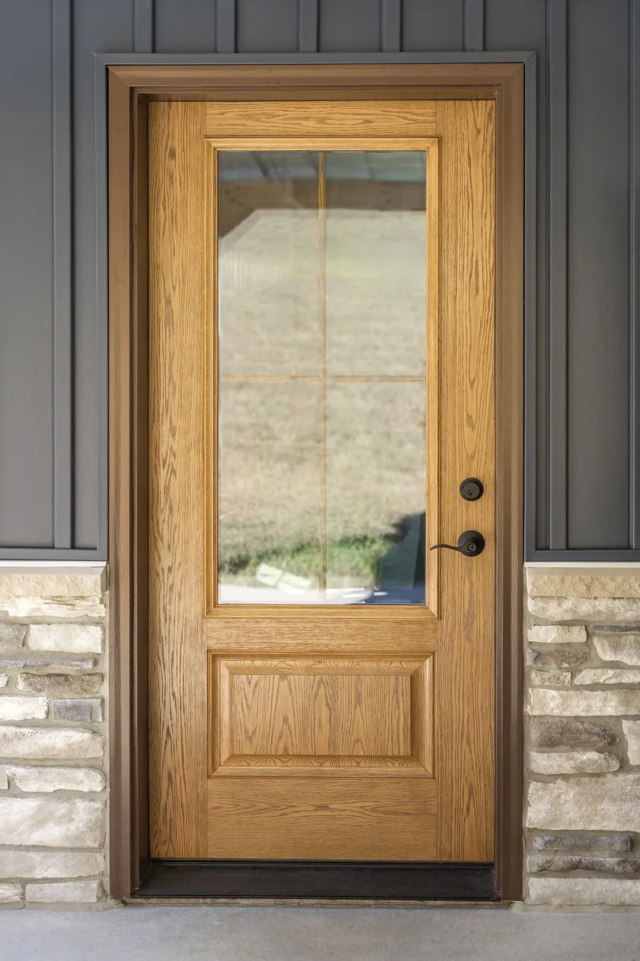 Wooden front door with glass panel, stone wall accents, and dark siding on a modern home exterior