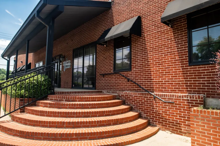 Curved brick staircase leading to entrance of red brick building with black awnings and metal railings.