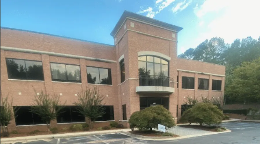 Modern three-story office building with large reflective glass windows and landscaped greenery on a cloudy day