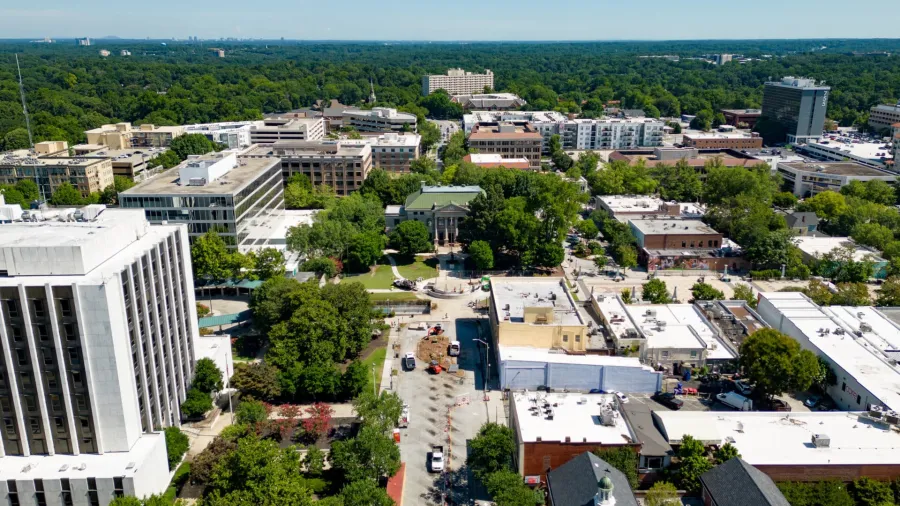 Aerial view of a cityscape with green trees, office buildings, and a clear blue sky on a sunny day.