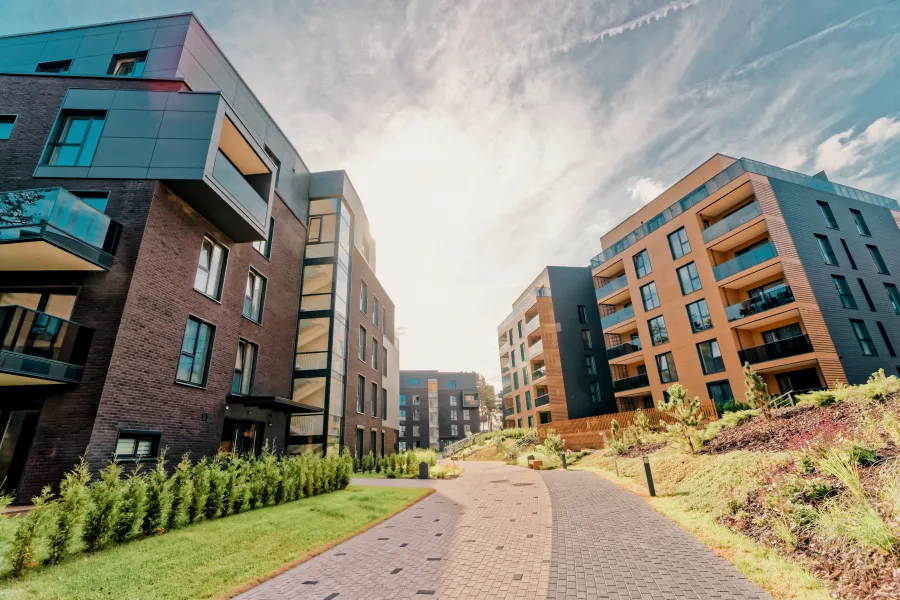 Modern apartment buildings with balconies lining a paved walkway under a bright sky in a landscaped urban area