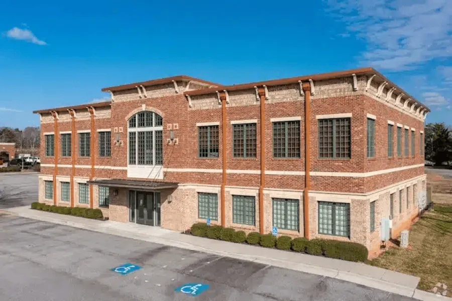 Two-story brick office building with large windows and handicap parking spaces under a blue sky.