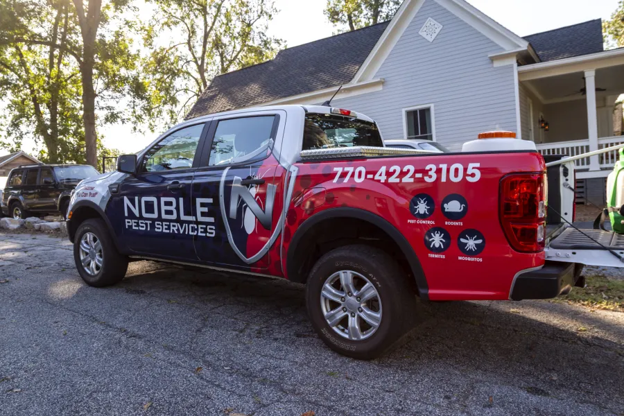 Noble Pest Services truck parked outside a house with company logo and contact number 770-422-3105 visible