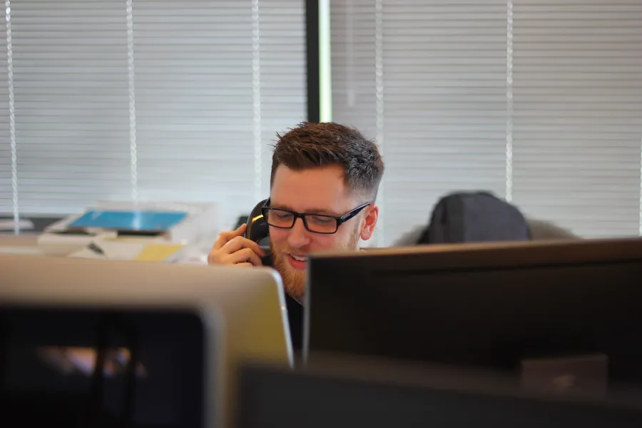 a man with a beard sitting at a desk with a phone