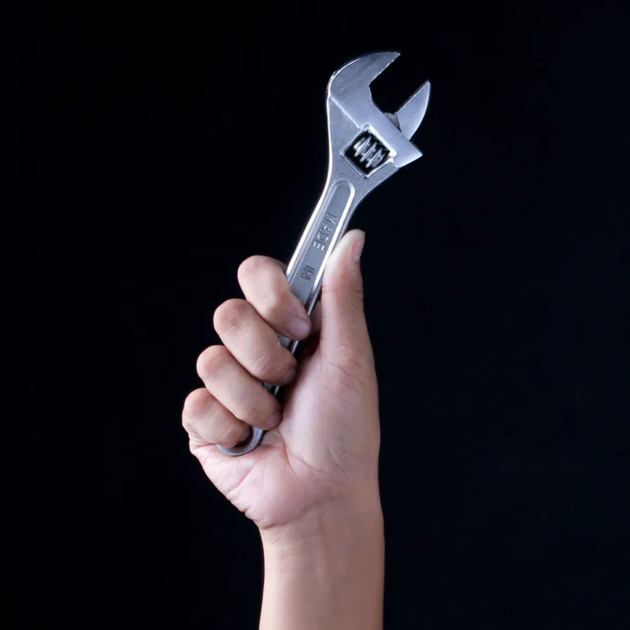Hand holding an adjustable wrench against a black background symbolizing repair and maintenance work.