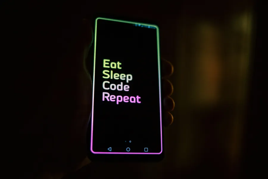 Hand holding smartphone with colorful neon text Eat Sleep Code Repeat on black screen