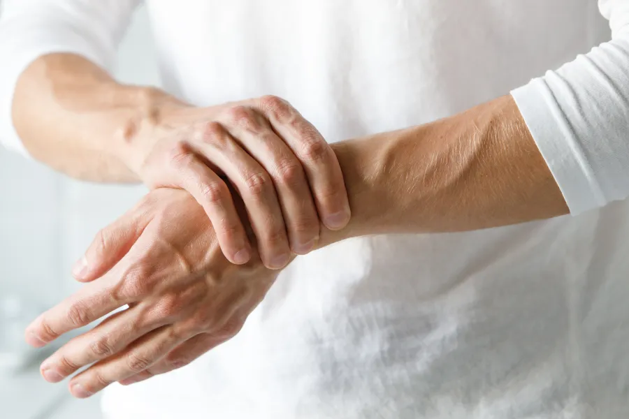 Man wearing white shirt holding wrist, showing pain or discomfort in wrist area.