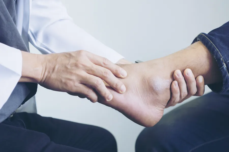 Doctor examining a patient's ankle for injury or pain in a clinical setting.
