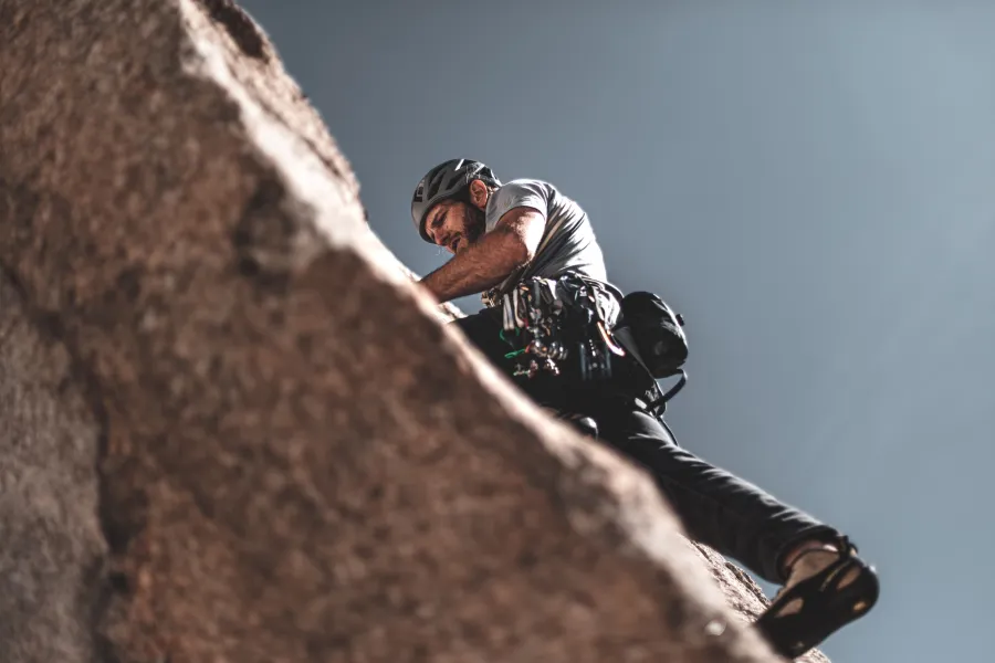 Man wearing helmet and climbing gear scaling a rocky cliff under clear blue sky