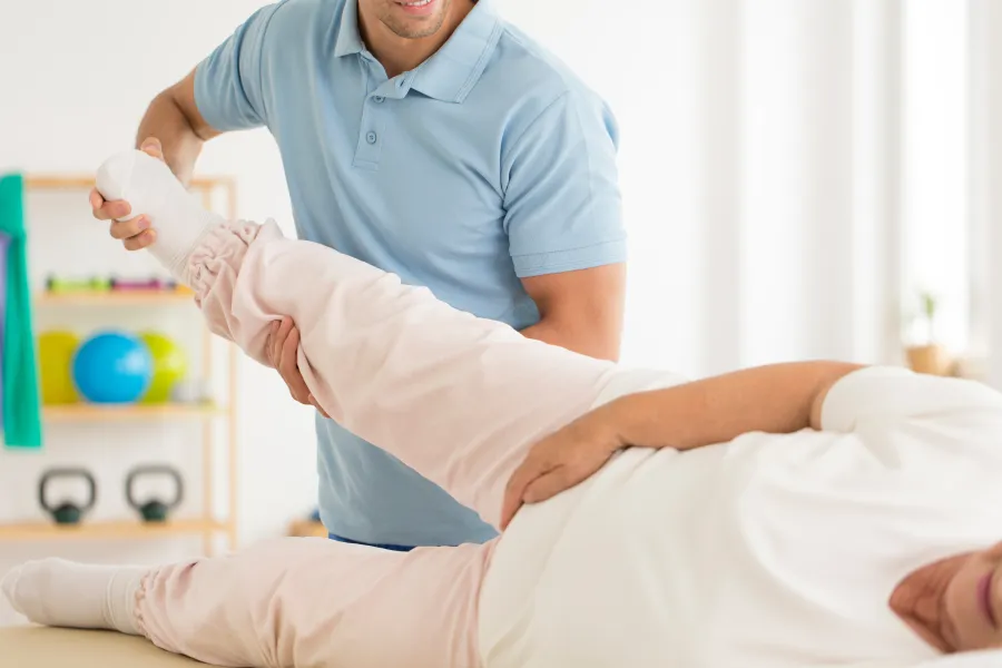 Physiotherapist assisting elderly woman with leg exercises in a bright rehabilitation setting