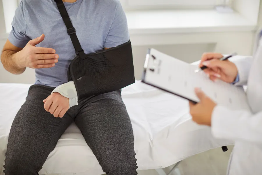Man with arm in sling consulting doctor taking notes on clipboard in medical office.