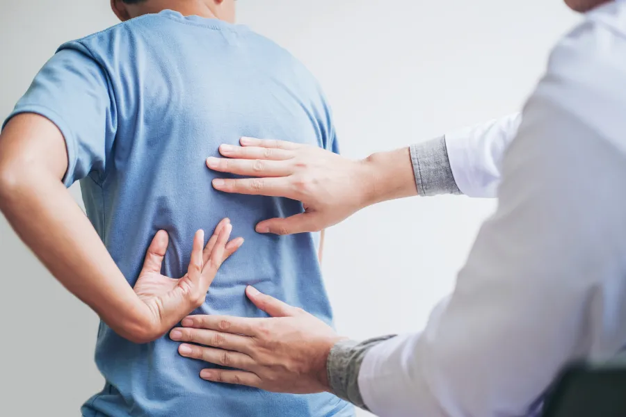 Doctor examining patient’s lower back pain with hands during a medical consultation in clinic.
