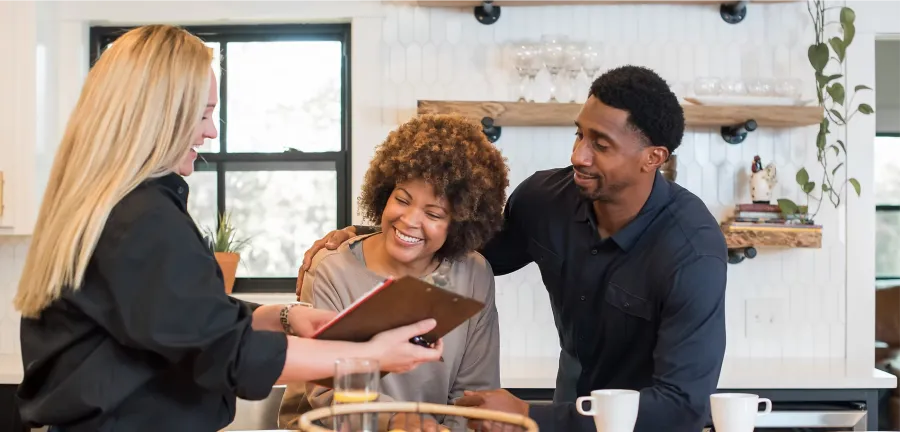 Couple smiling and reviewing a menu with a server in a modern kitchen setting with drinks on the counter