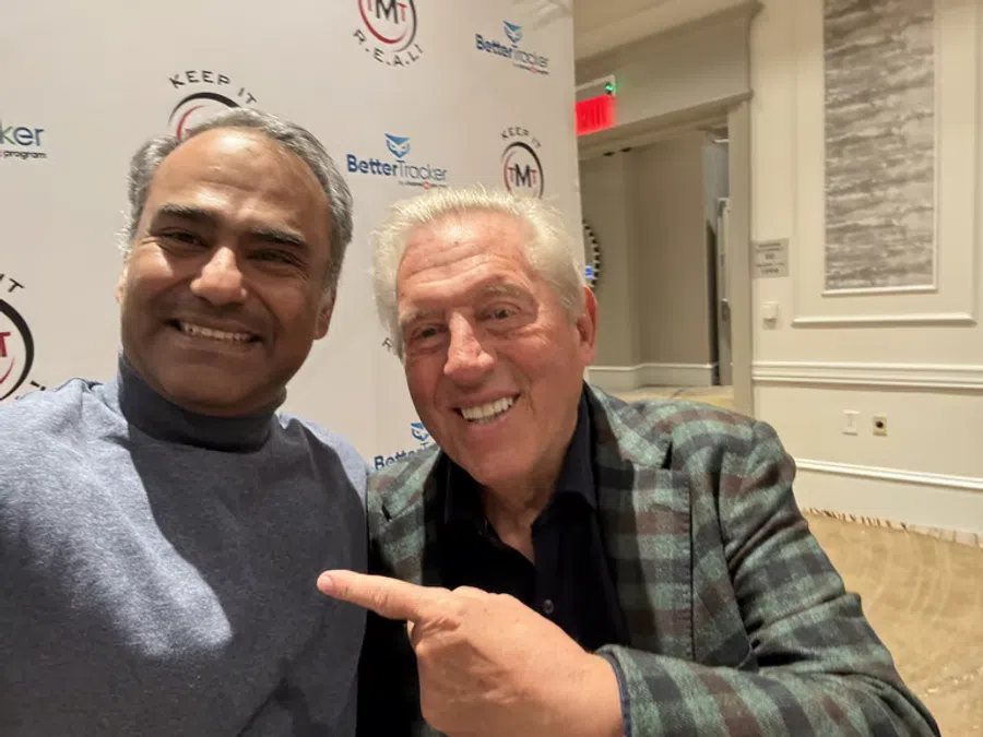 Two men smiling at a conference with branded backdrop for Keep It R.E.A.L. and Better Tracker.