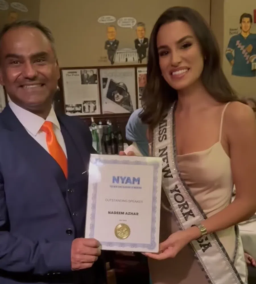 Man in suit with orange tie and Miss New York USA holding an outstanding speaker certificate from NYAM.
