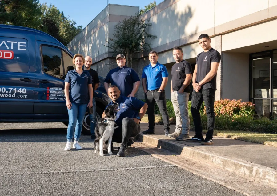 Team of seven workers with a dog posing outside a service van and building on a sunny day