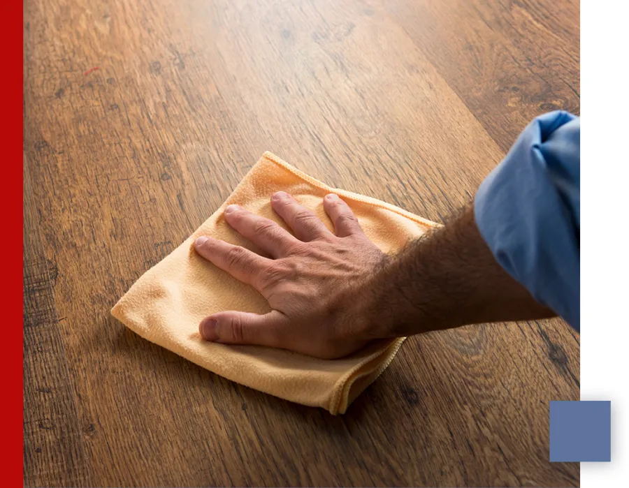 Hand wiping a wooden surface with a yellow microfiber cloth for cleaning and polishing.
