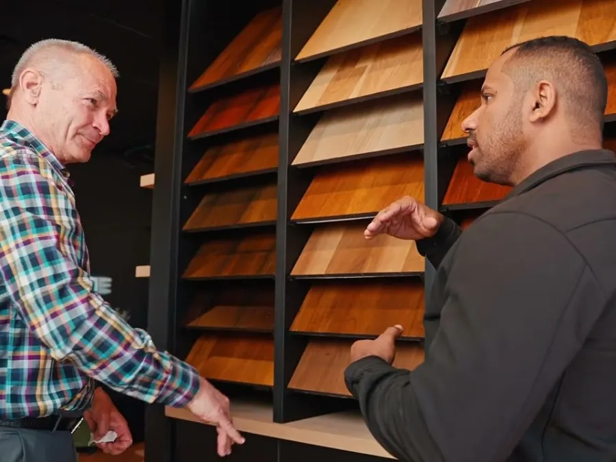 Two men discussing various wood flooring samples displayed on shelves in a showroom.