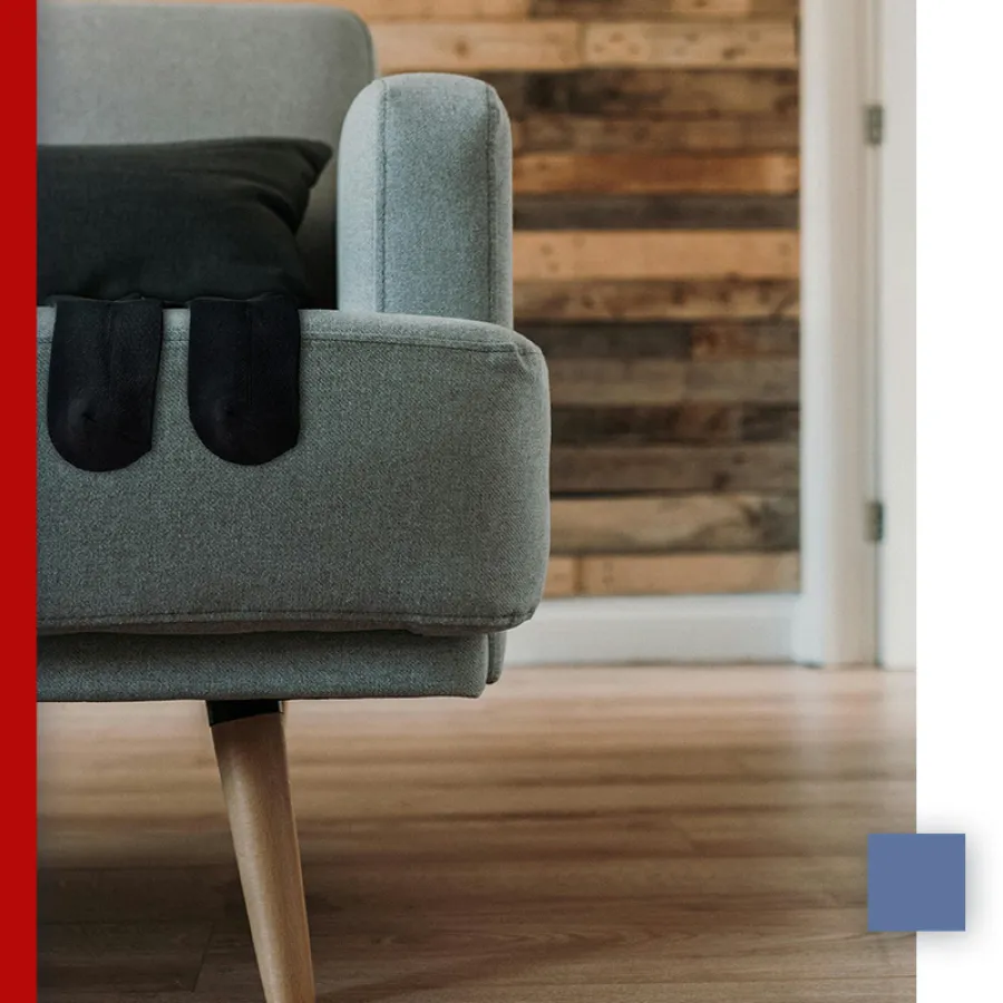Close-up of grey sofa arm with black socks draped over it, wooden floor and rustic wood wall background.